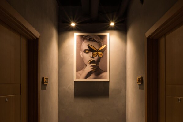Un pasillo con una obra enmarcada en la pared, puertas a ambos lados y un cartel con un número sobre cada puerta.