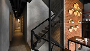 A modern interior with a staircase, a brick wall with shelves, and a table with a plate and cup. - Cove W Suites (Jakarta)