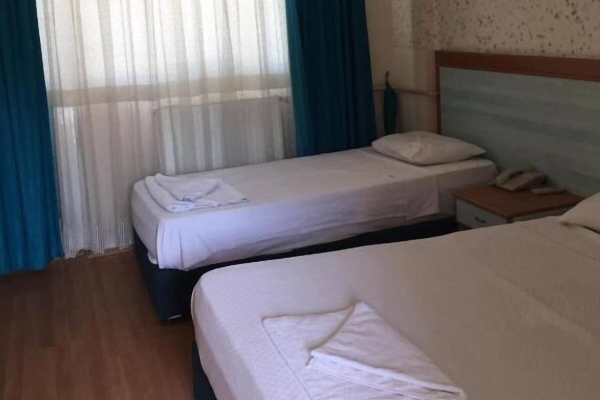 A hotel room with two beds, a wooden floor, a window with curtains, and a nightstand with a phone.