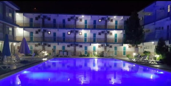 Relax by the pool with lounge chairs and umbrellas, surrounded by hotel rooms with balconies.