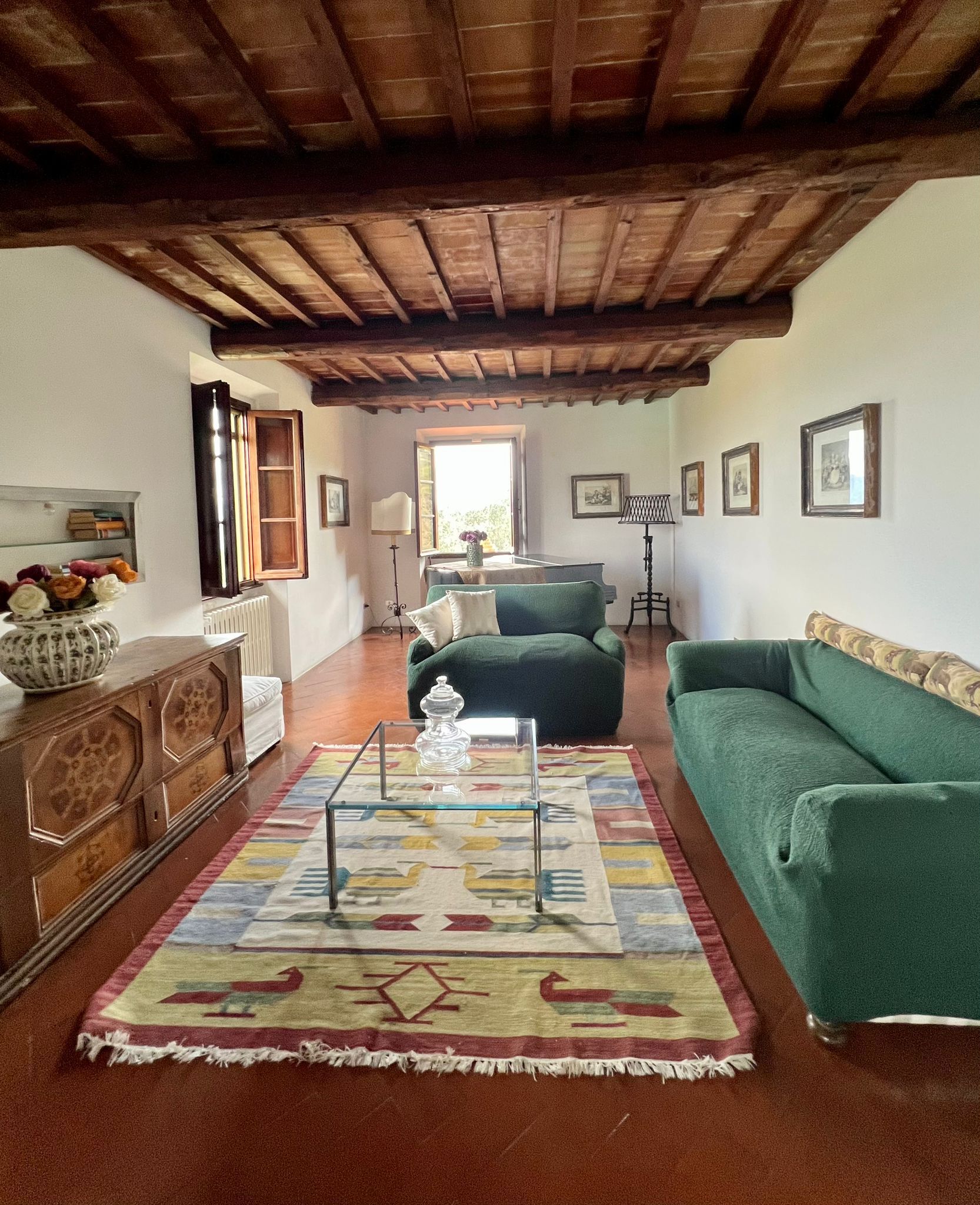Una sala de estar acogedora con un sofá verde, un aparador de madera, un tapete estampado y techo de madera.