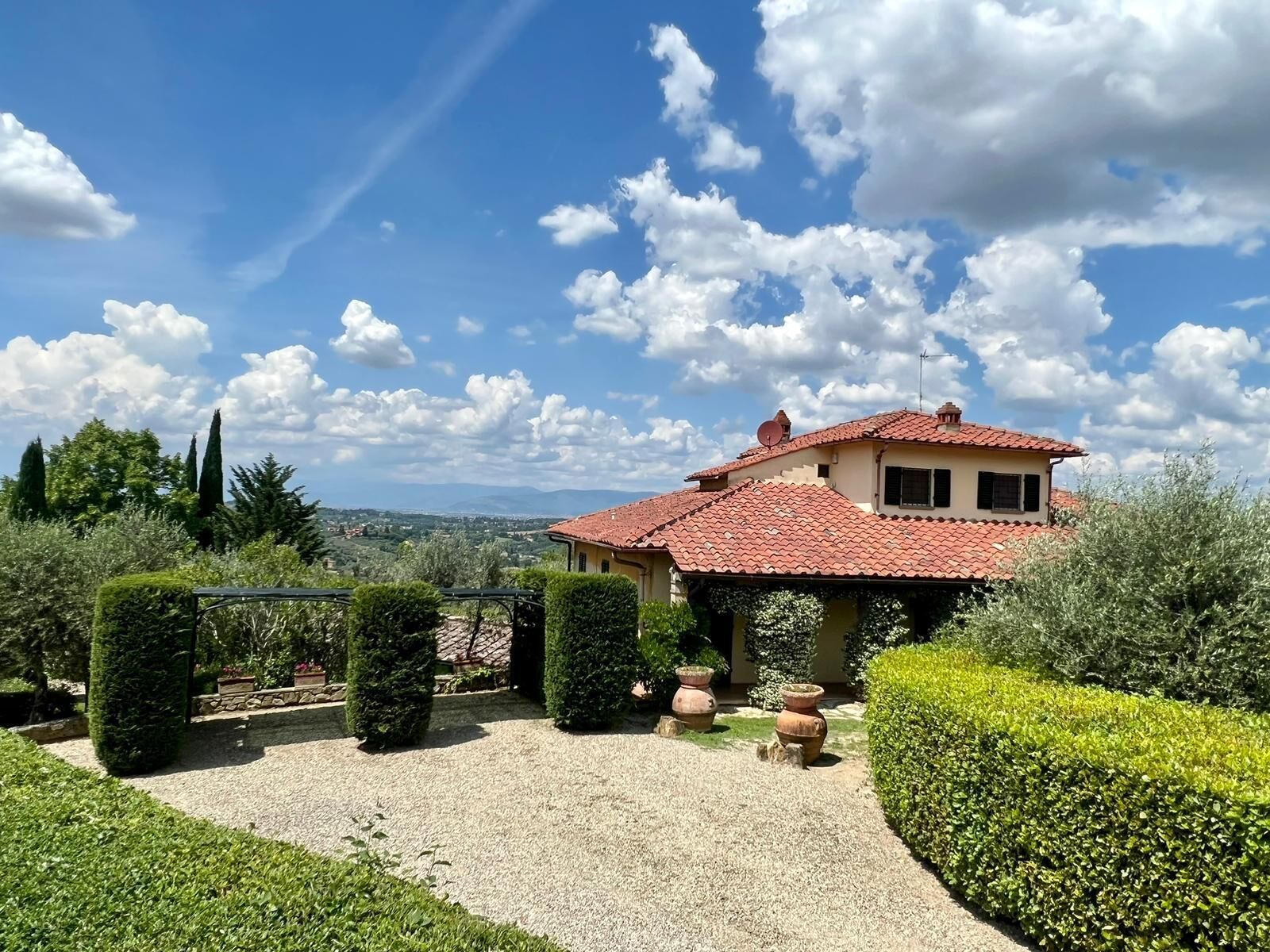 A villa with a red-tiled roof, surrounded by well-manicured hedges and gravel paths.