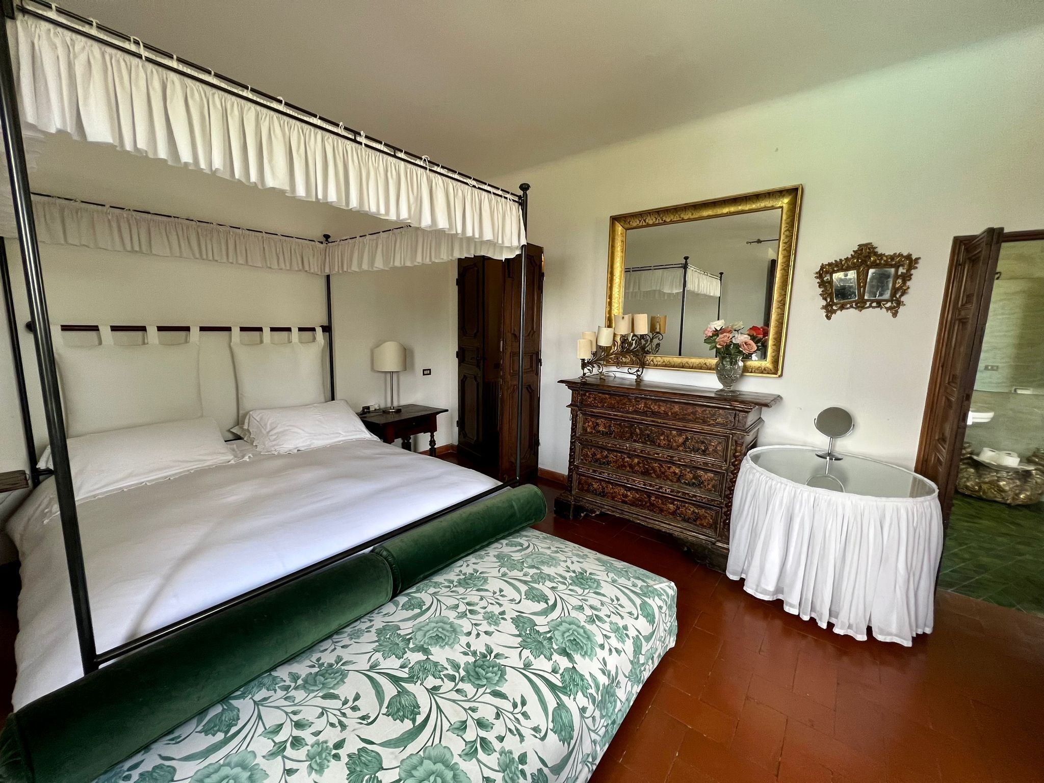 A four-poster bed with a canopy, a dresser with a mirror, and a round table with a lamp.
