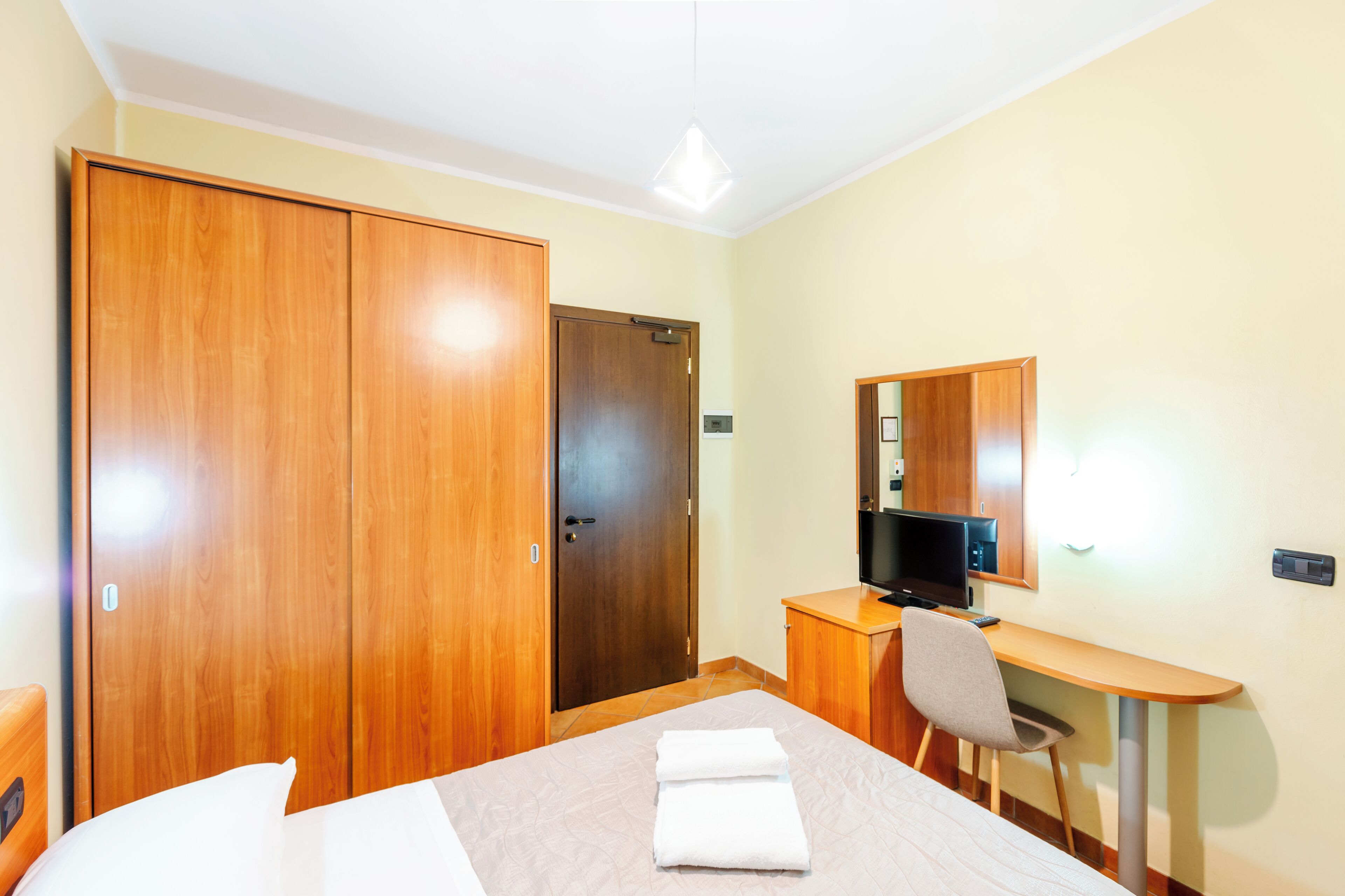 A hotel room with a bed, a desk with a chair, a television, and a wardrobe.
