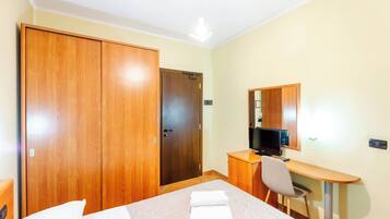 Una habitación de hotel con cama, escritorio con silla, televisión y armario.