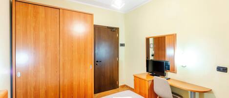 A hotel room with a bed, a desk with a chair, a television, and a wardrobe.