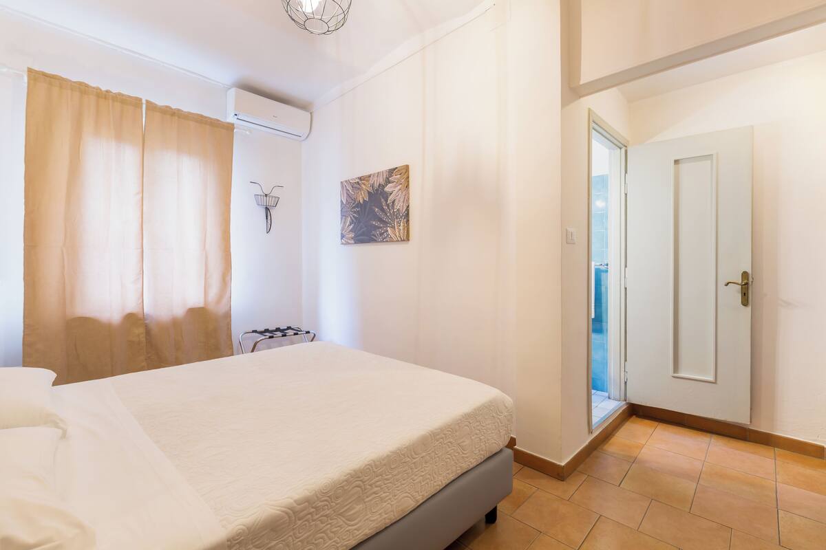 A bedroom with a bed, a bicycle, a wall-mounted basket, and a door leading to a balcony.