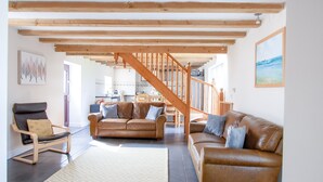 Amplia sala de estar con escalera de madera, sofás de cuero y alfombra estampada.