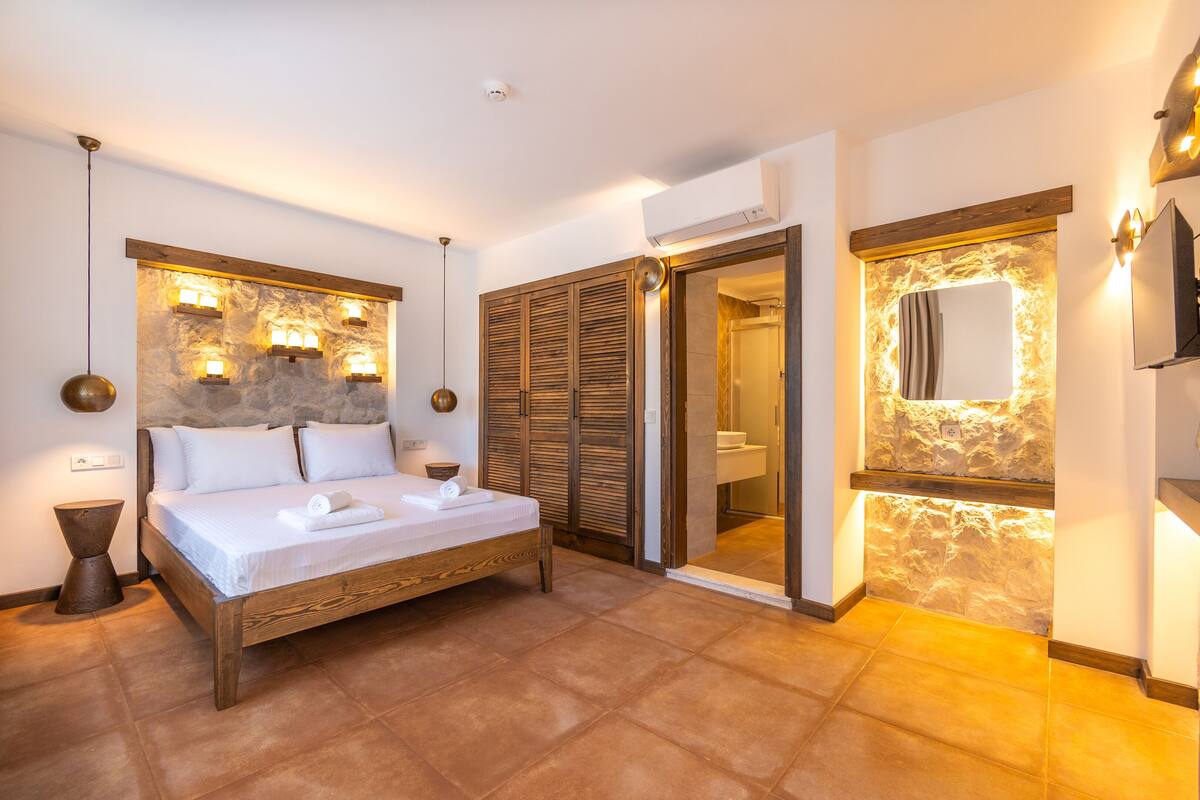 Ein Schlafzimmer mit einem hölzernen Bett, einer Steinwand und einem Badezimmer mit Spiegel.
