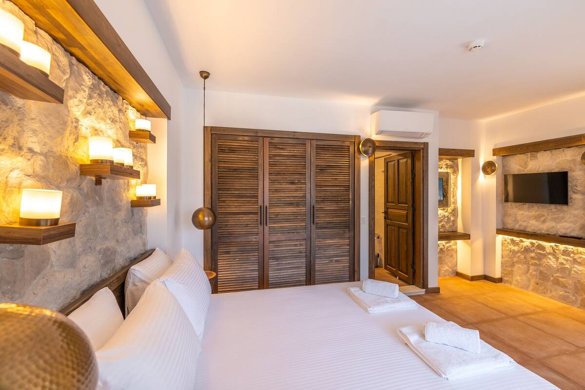 Ein Hotelzimmer mit einem großen Bett, einem Holzschrank, Wandverkleidungen aus Stein und einem an der Wand befestigten Flachbildfernseher.