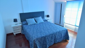 Un dormitorio con una cama grande, una mesita de noche, una lámpara y una ventana con persianas.