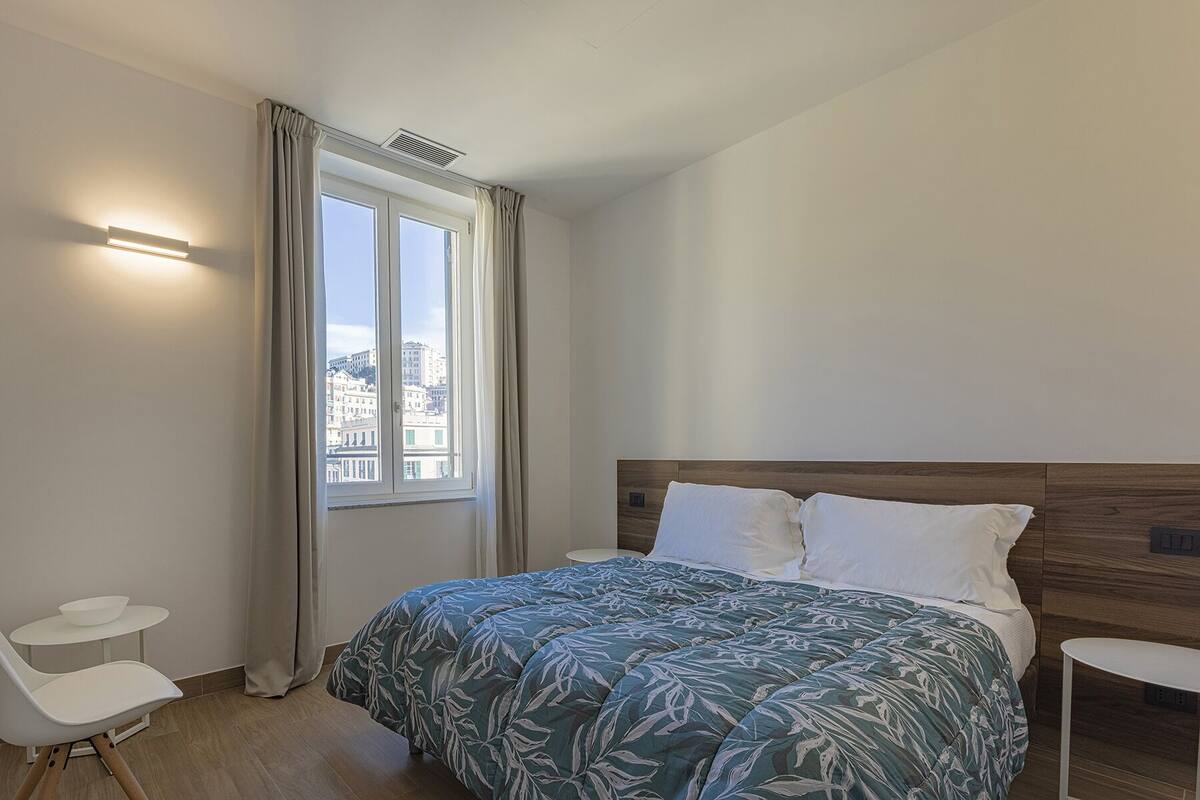 A bedroom with a bed, a chair, a small table, and a window with curtains.
