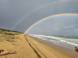 A beach with a rainbow, sandy dunes, and waves.