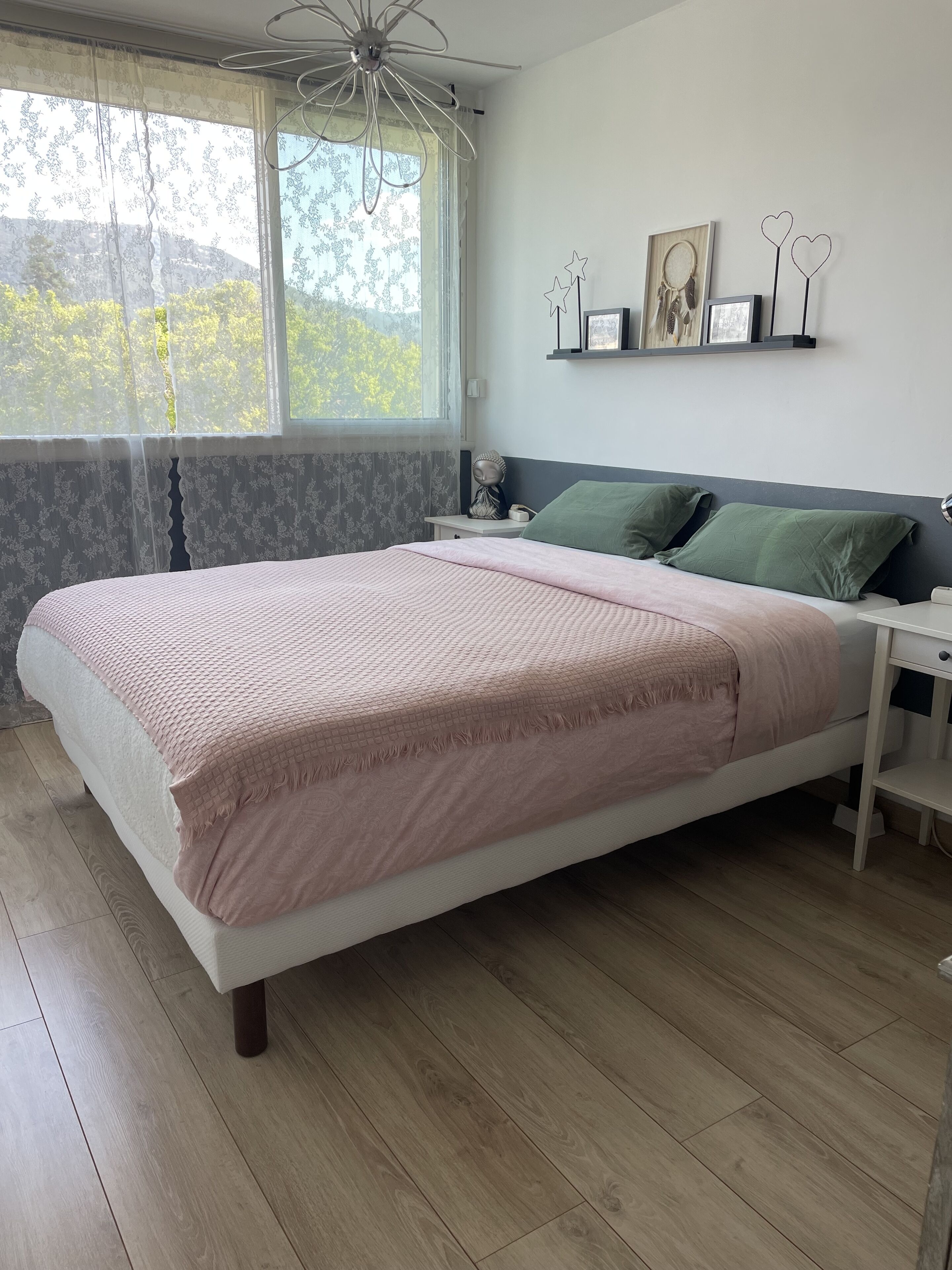 A bedroom with a bed, a nightstand, a window with curtains, and wall decorations.