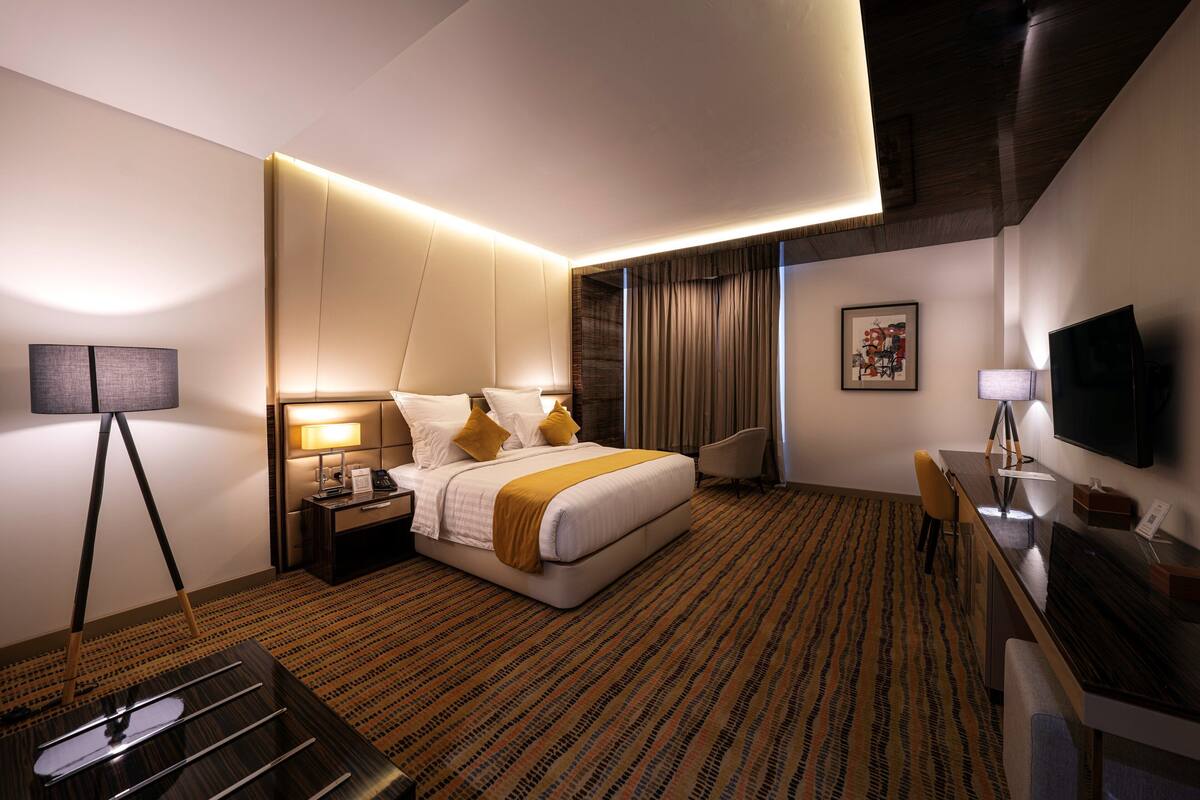 A hotel room with a bed, bedside table, lamp, desk, chair, and a television.