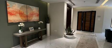 Un interior moderno con suelo de mármol, un banco, una planta en maceta y un cuadro abstracto de gran tamaño.