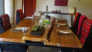 A long wooden dining table with black chairs, red plaid curtains, and a sign on the wall. - emayian geust house (Maasai Mara)