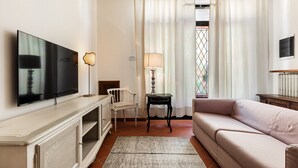 Un salon équipé d’un téléviseur à écran plat, d’un canapé, d’un fauteuil, d’une lampe et d’une fenêtre avec des rideaux.