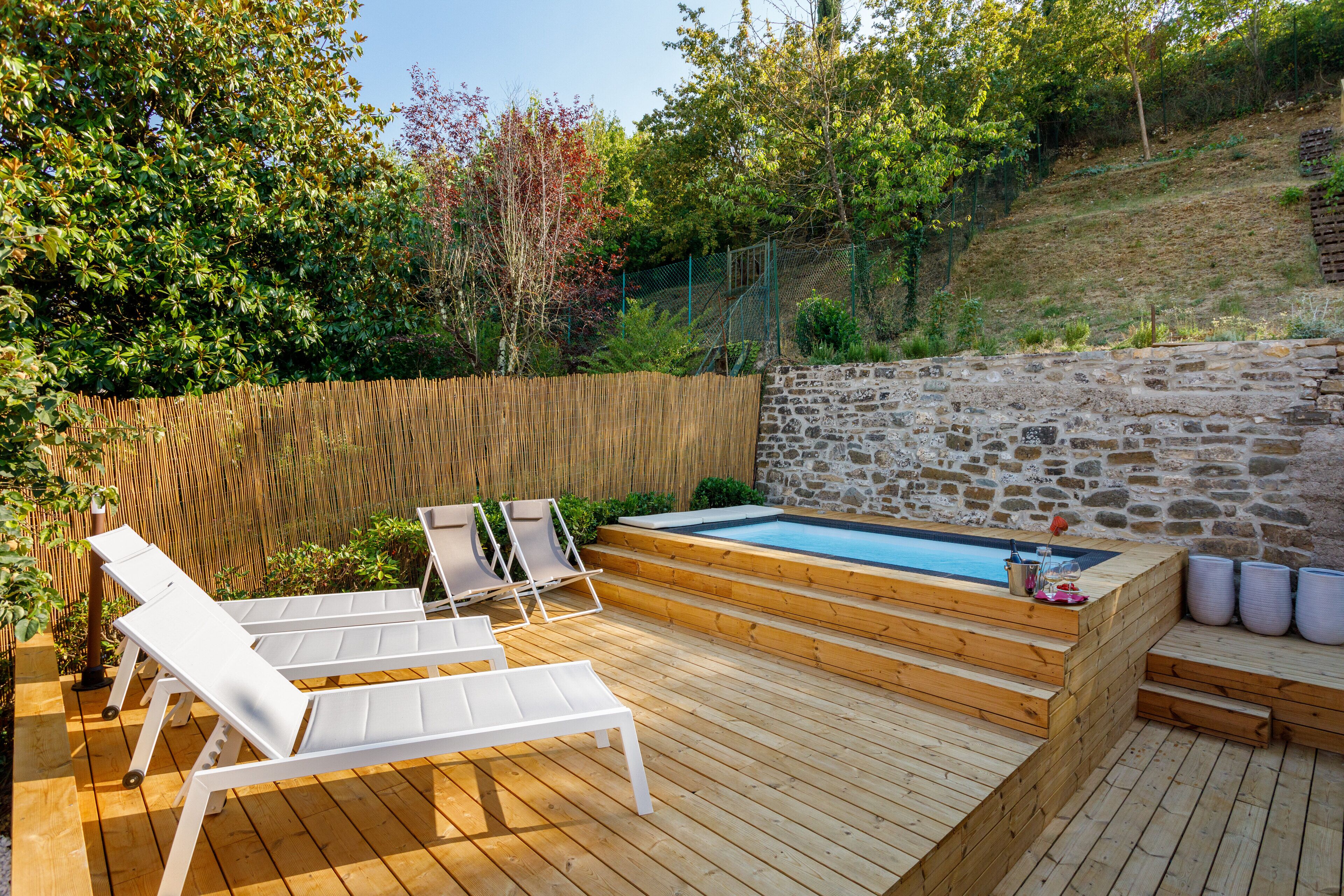 A wooden deck with a stone wall, a hot tub, and white lounge chairs.
