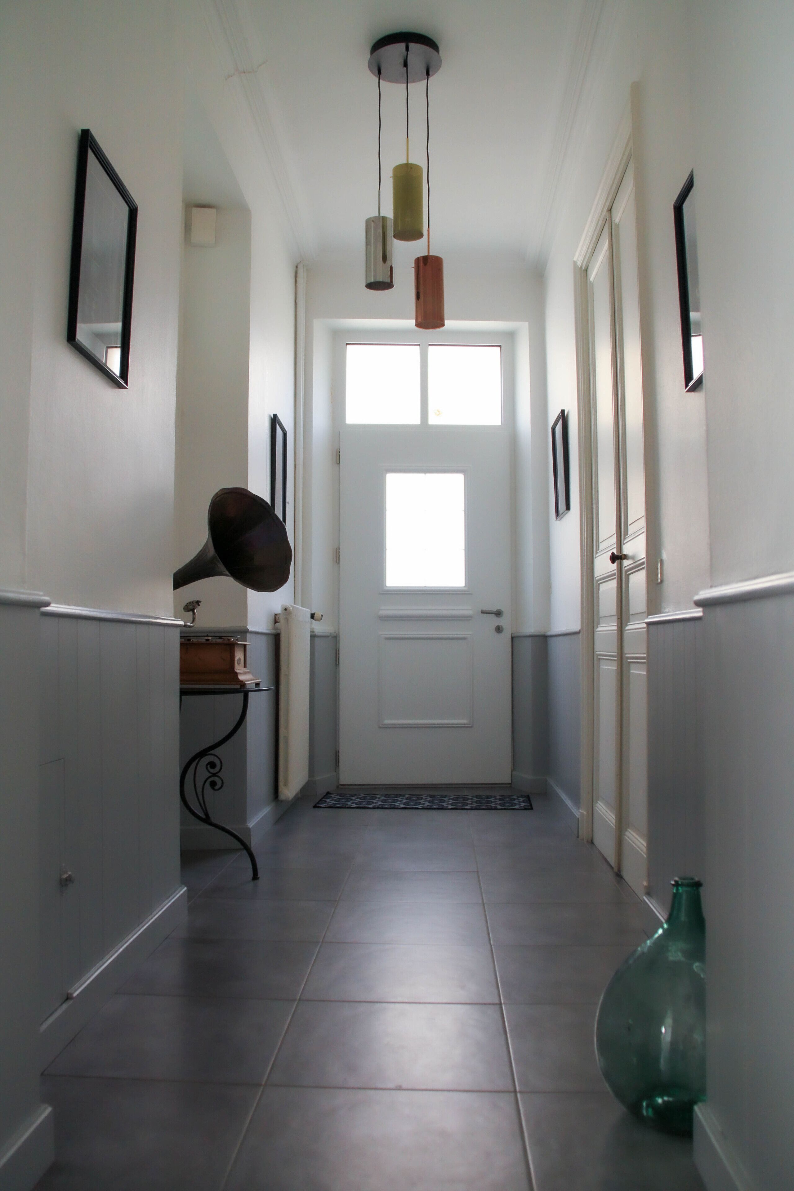 A hallway with a white door, a hanging light fixture, and a green vase on the floor.