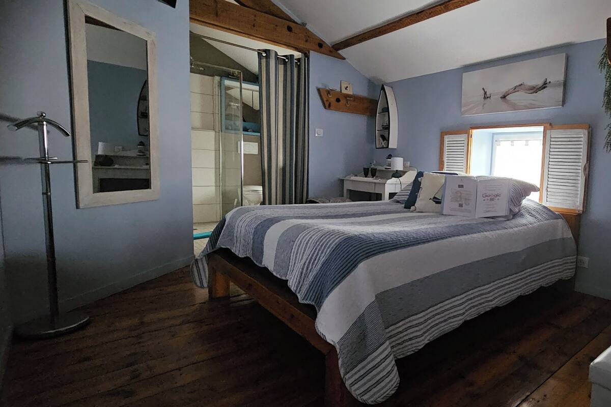 A bedroom with a bed, a desk, a chair, a window, and a mirror.