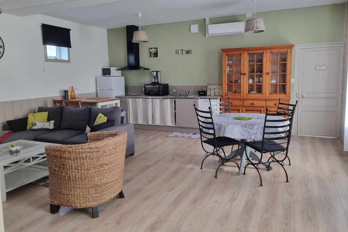 A compact living space with a sofa, dining table, wicker chair, kitchenette, and a cabinet.