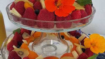 A two-tiered glass fruit stand with strawberries, blueberries, kiwi, and melon slices.