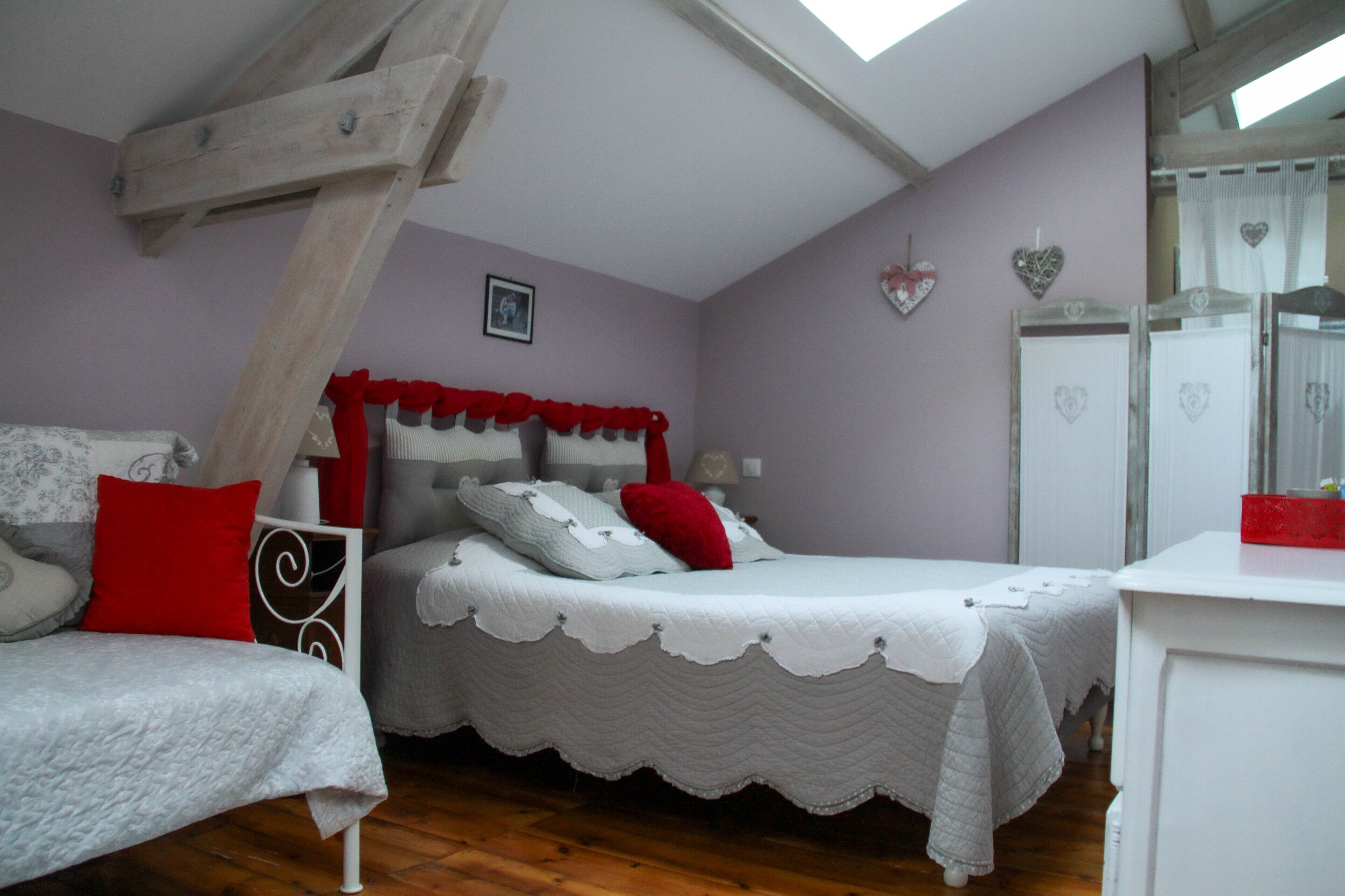 Une chambre avec un plafond en pente, un lit doté d’une tête de lit blanche et rouge, une table de chevet et une commode.