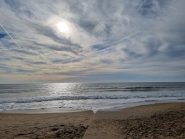 Una playa con huellas que conducen al agua, cielo despejado y el sol brillando.