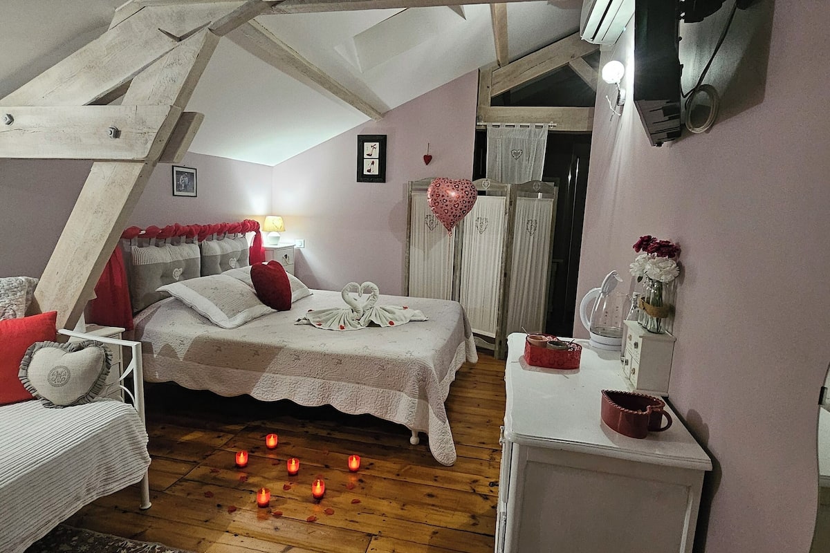 A cozy bedroom with a sloped ceiling, a bed with a white bedspread, a bedside table with a lamp, and a mirror.