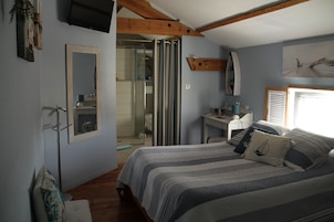 Un dormitorio con cama, escritorio, silla, espejo y zona de ducha.