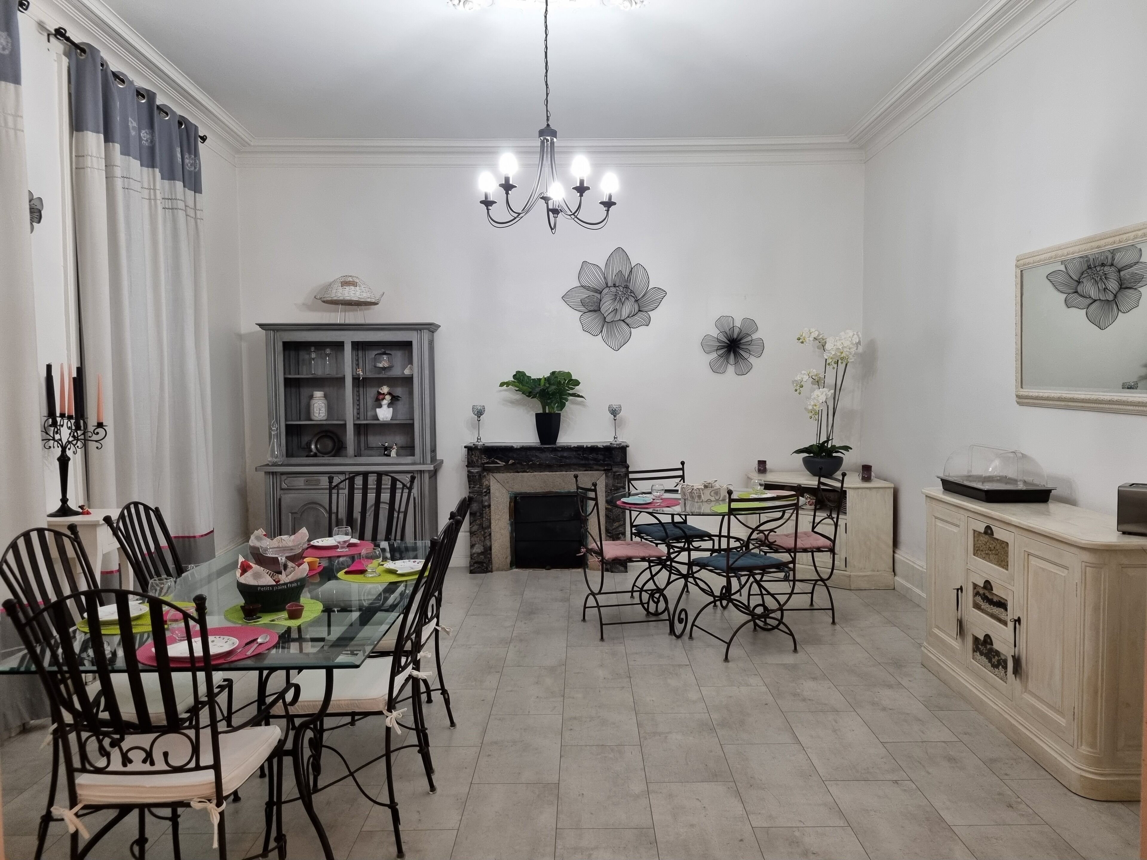 A dining room with a glass table, black metal chairs, a chandelier, a fireplace, and wall art.