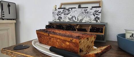 Una hogaza de pan sobre un plato blanco con un asa negra, una tostadora y un objeto decorativo con motivos florales.