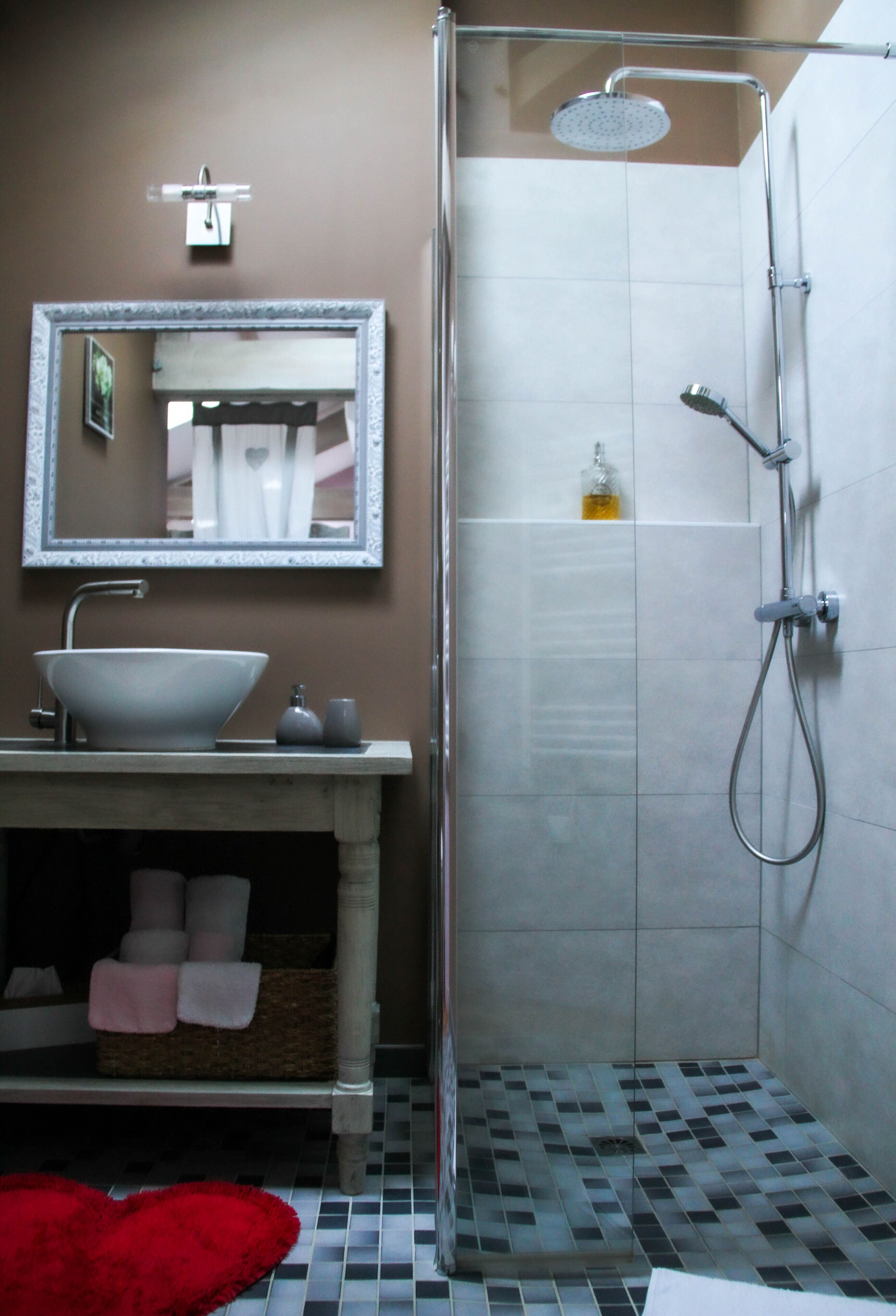 A bathroom with a white sink, a mirror, a shower, and a tiled floor.