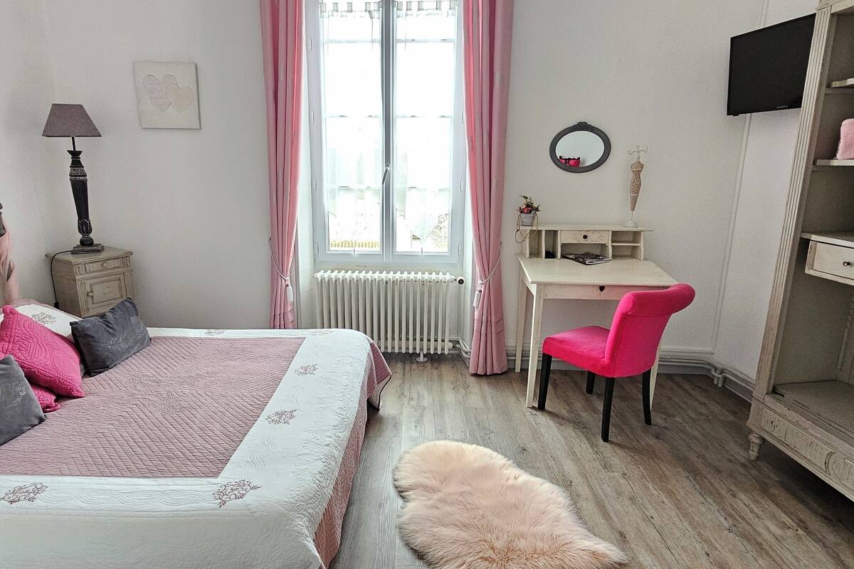 A bedroom with a bed, a desk, a chair, a wardrobe, a radiator, and a window with curtains.