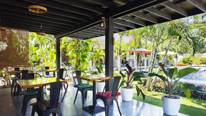 An outdoor seating area with tables and chairs, surrounded by lush greenery and a pool. - ohana panglao resort (Panglao)