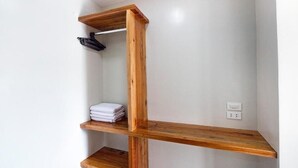 A corner with a wooden shelf unit against a white wall, holding folded towels and a black garment. - ohana panglao resort (Panglao)