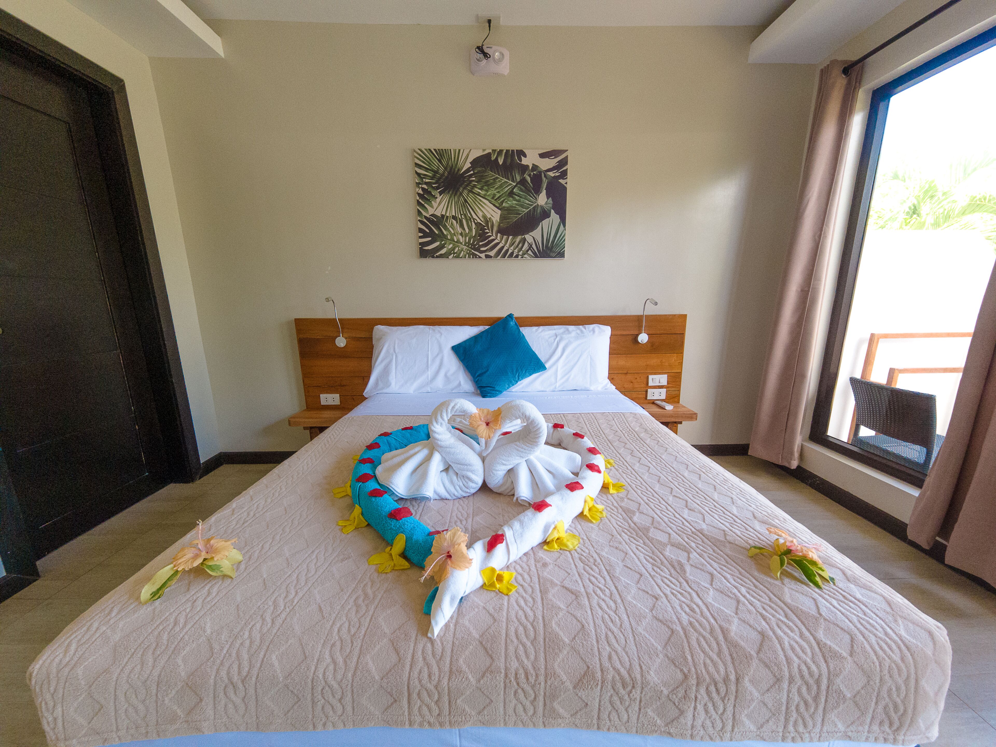 A hotel room with a bed, a wooden headboard, a wall-mounted painting, and a window with curtains.