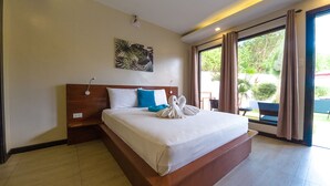 A hotel room with a large bed, a headboard, a wall-mounted artwork, a window with curtains, and a view of greenery outside. - ohana panglao resort (Panglao)