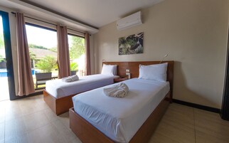 A hotel room with two beds, a large window with curtains, an air conditioning unit, and a painting on the wall.