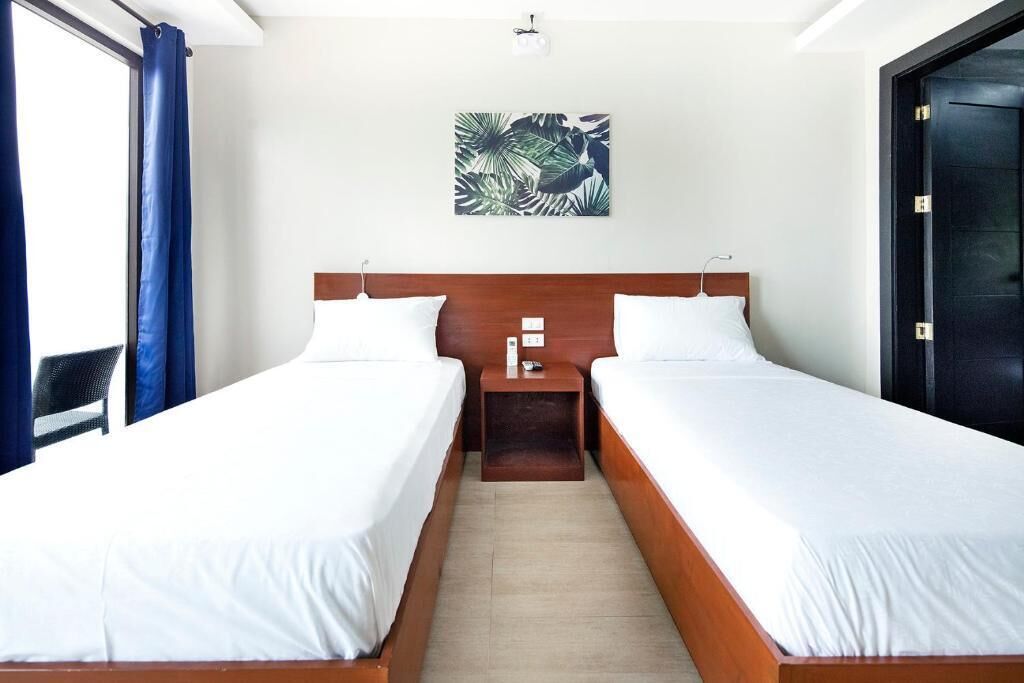 Ett hotellrum med två separata sängar, en sänggavel i trä, ett nattduksbord och en väggdekoration med tropiskt tema.