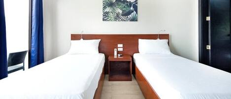 Ett hotellrum med två separata sängar, en sänggavel i trä, ett nattduksbord och en väggdekoration med tropiskt tema.