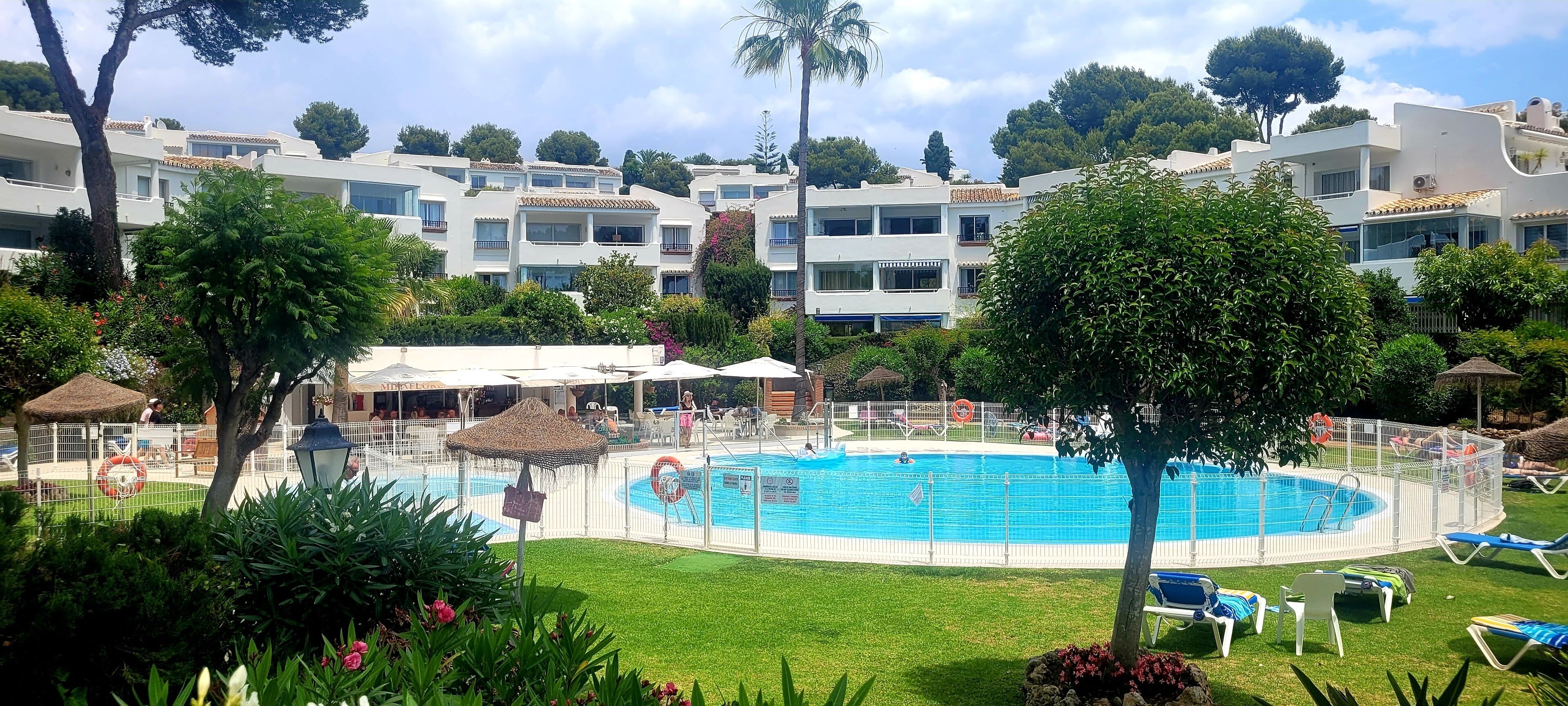 A swimming pool surrounded by a white fence, with lounge chairs and umbrellas.