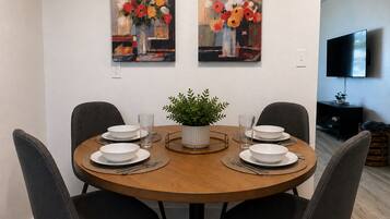 A dining area with a round wooden table, four chairs, and two paintings above the table.