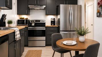 A modern kitchen with dark cabinets, stainless steel appliances, a wooden dining table, and a small potted plant.