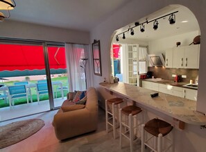 Una cocina moderna con barra, armarios blancos y un amplio ventanal con vistas a un espacio exterior arbolado.