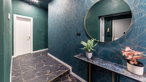 A hallway with a marble floor, a green wall with a leaf pattern, a round mirror, and two potted plants.