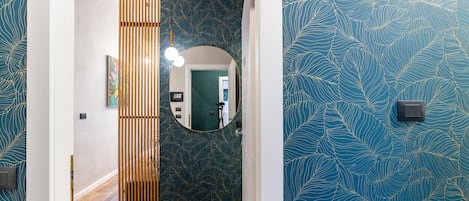 Un pasillo con un separador de listones de madera, un espejo redondo y un revestimiento de pared estampado.