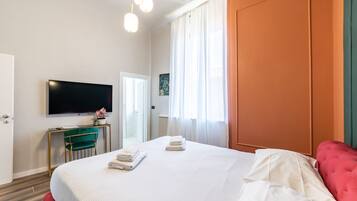 A hotel room with a large bed, a flat-screen TV, a desk with a chair, and a window with curtains.