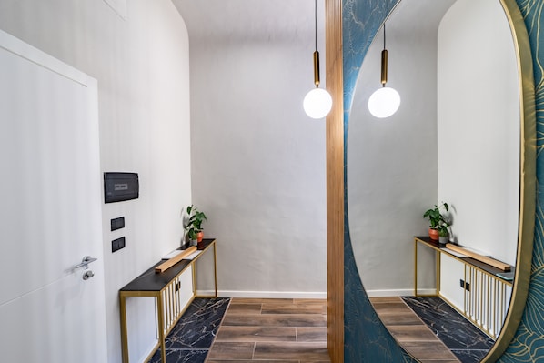 A modern hallway with a wooden console table, a potted plant, and a mirror reflecting the space.